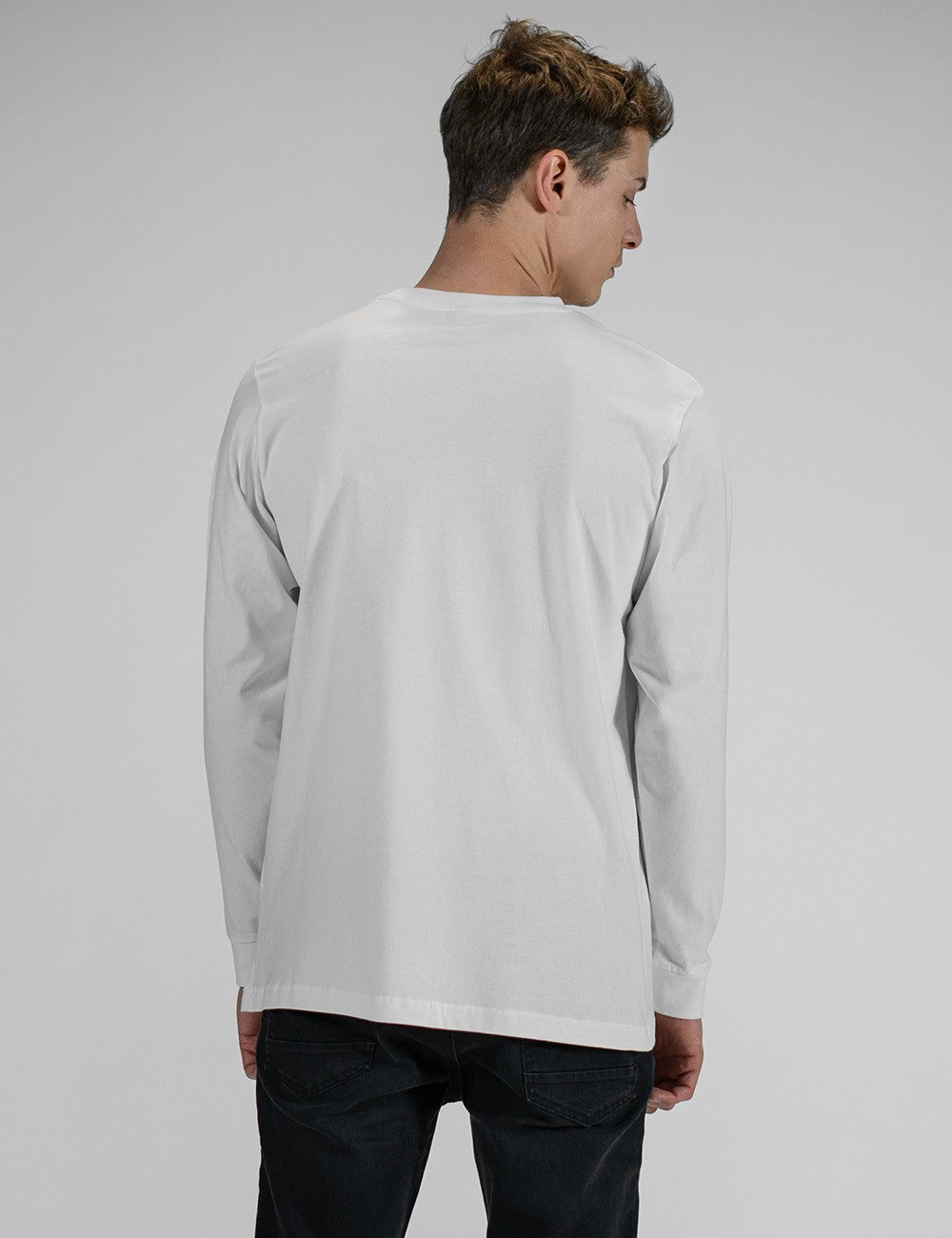 A young man wearing a white long-sleeve crewneck shirt. He has paired the shirt with slim-fit dark black jeans.