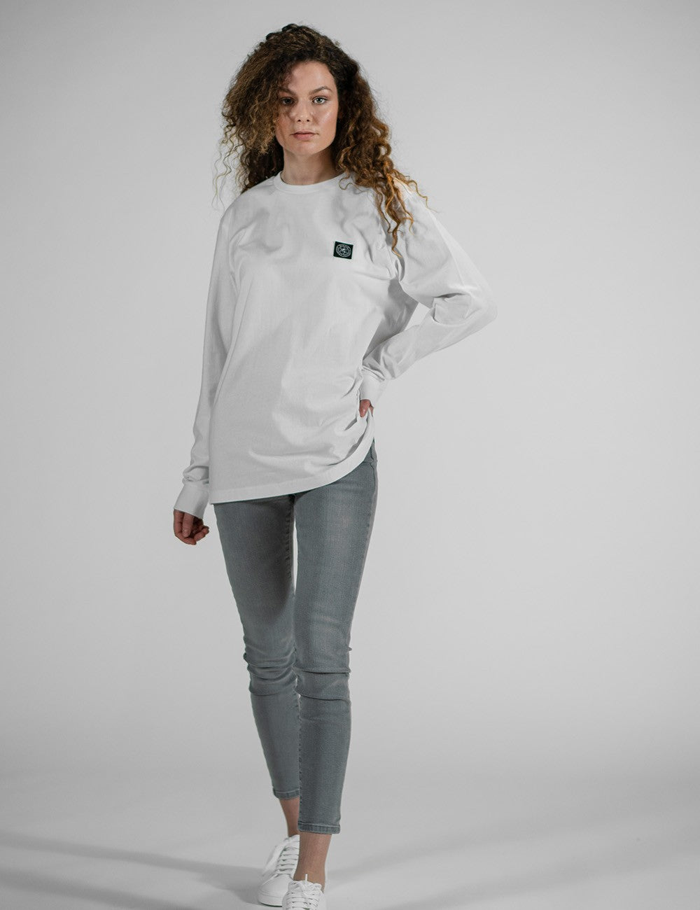 Model wearing a Rocket Science white long-sleeve crewneck shirt with a black 
chest logo patch. 