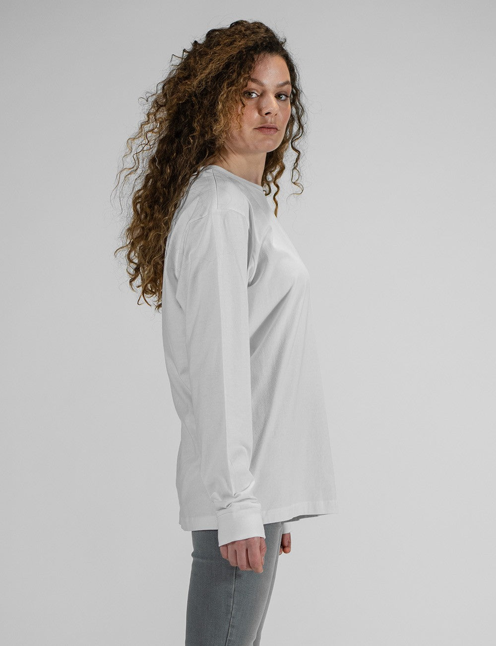 Model wearing a Rocket Science white long-sleeve crewneck shirt with a chest logo patch. 