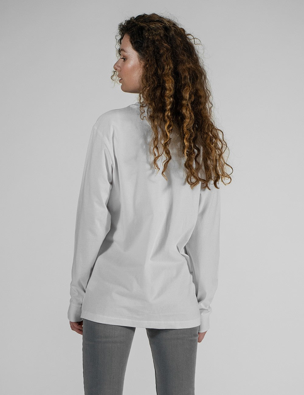 A model modeling the Rocket Science unisex white long-sleeve t-shirt with ribbed cuffs, styled casually with slim grey jeans.