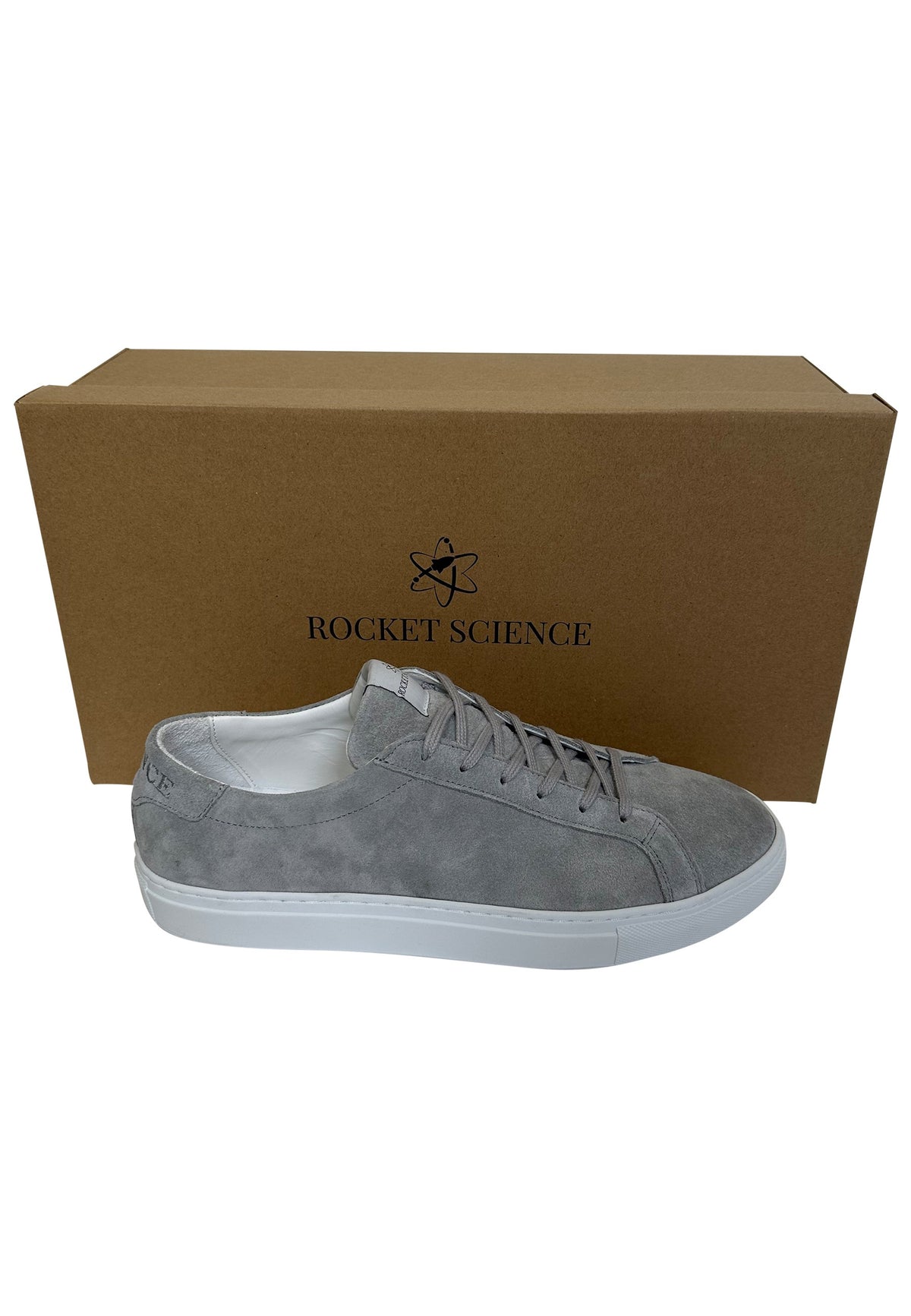 A gray suede low-top sneaker with a white sole, positioned in front of its brown cardboard packaging box which features the Rocket Science logo.