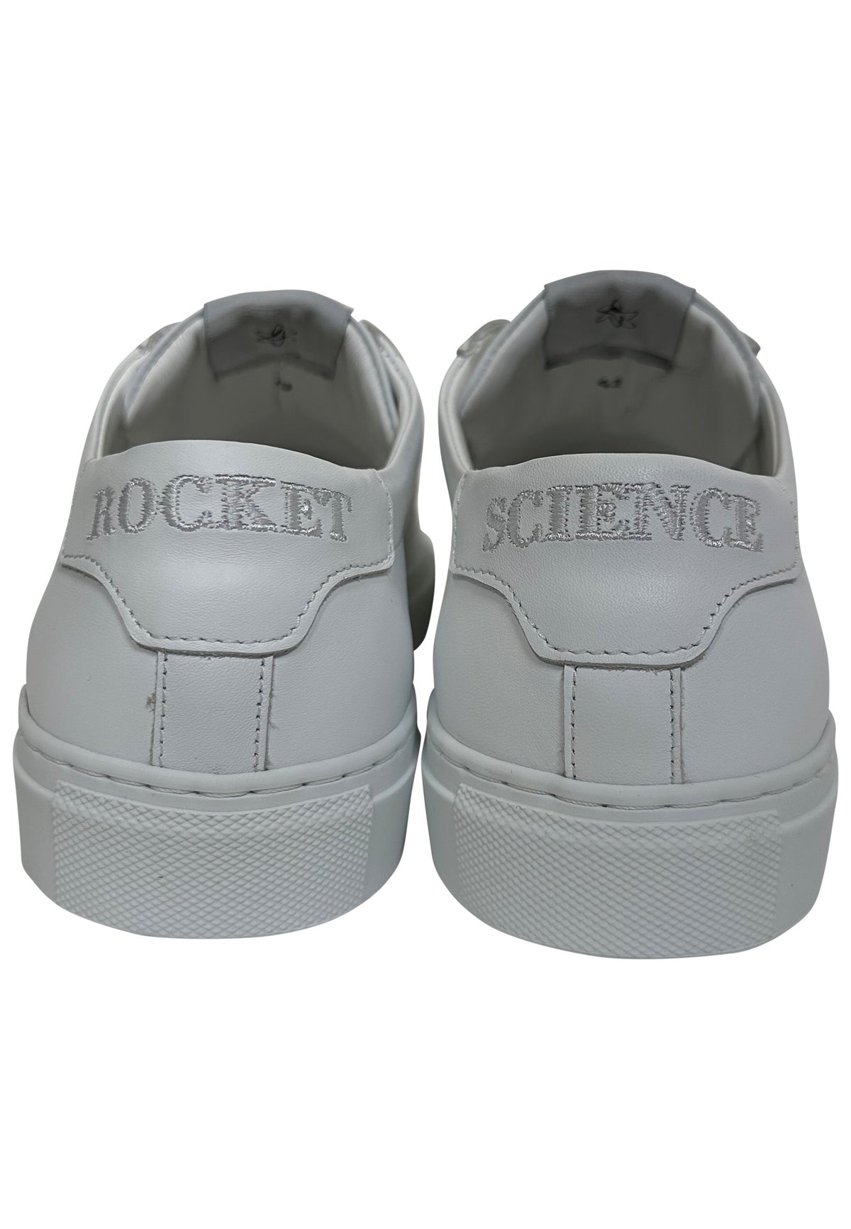 A pair of white low-top sneakers shown from the back, featuring the words 'ROCKET' and 'SCIENCE' in silver glitter lettering on the heel panels.