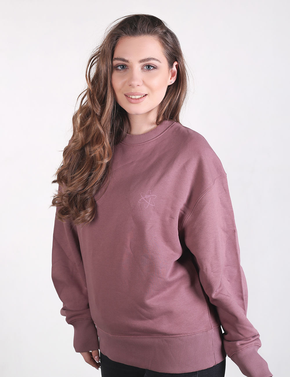 A woman with long, wavy brown hair smiling while wearing a mauve crewneck sweatshirt.