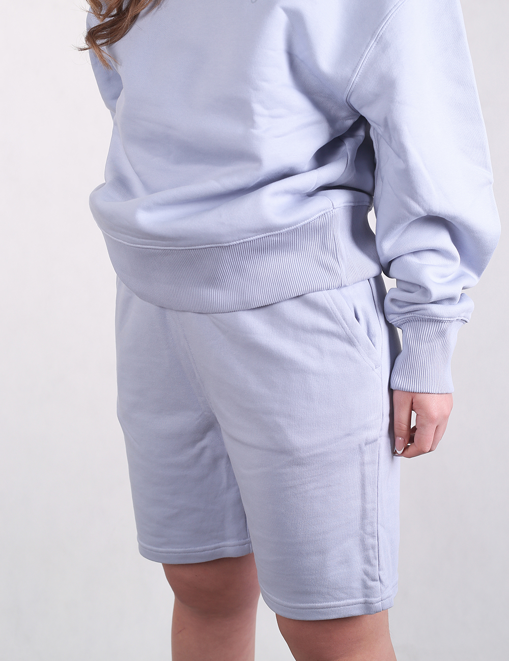 A person wearing a matching light blue loungewear set, consisting of a thick, oversized crewneck sweatshirt and comfortable fleece sweatshorts with side pockets.