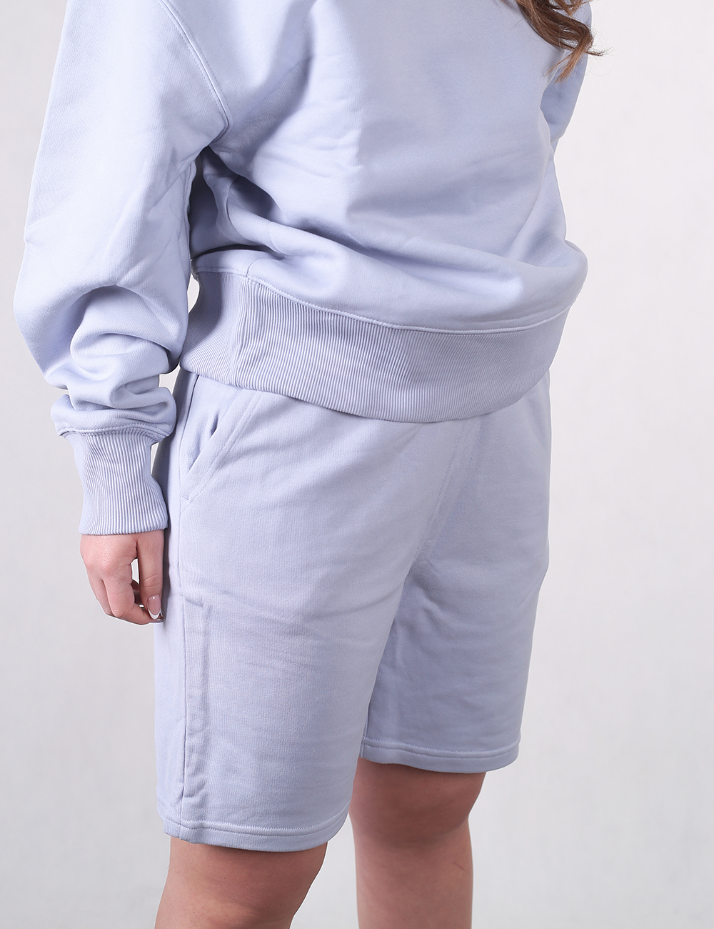 A person wearing a matching light blue loungewear set, consisting of a thick, oversized crewneck sweatshirt and comfortable fleece sweatshorts with side pockets.