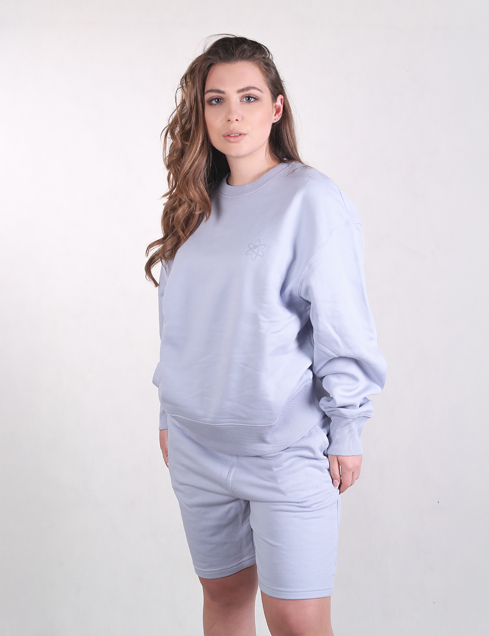 A woman wearing a matching, monochromatic light blue loungewear set consisting of an oversized crewneck sweatshirt and fitted, mid-thigh length shorts.