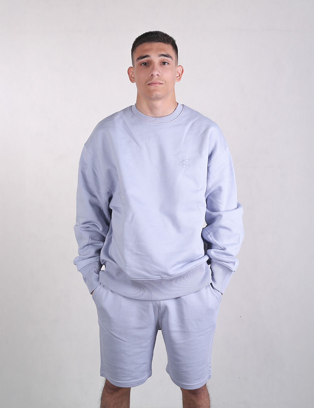 A man wearing light blue Rocket Science organic cotton sweat shorts with hands in his pockets.