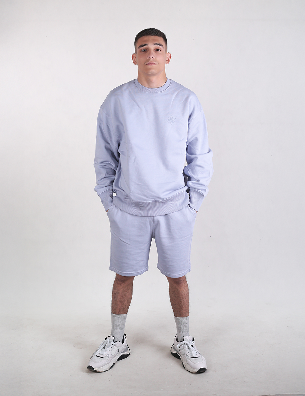 A man wearing light blue Rocket Science organic cotton sweat shorts with hands in his pockets.