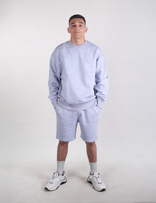A man wearing light blue Rocket Science organic cotton sweat shorts with hands in his pockets.