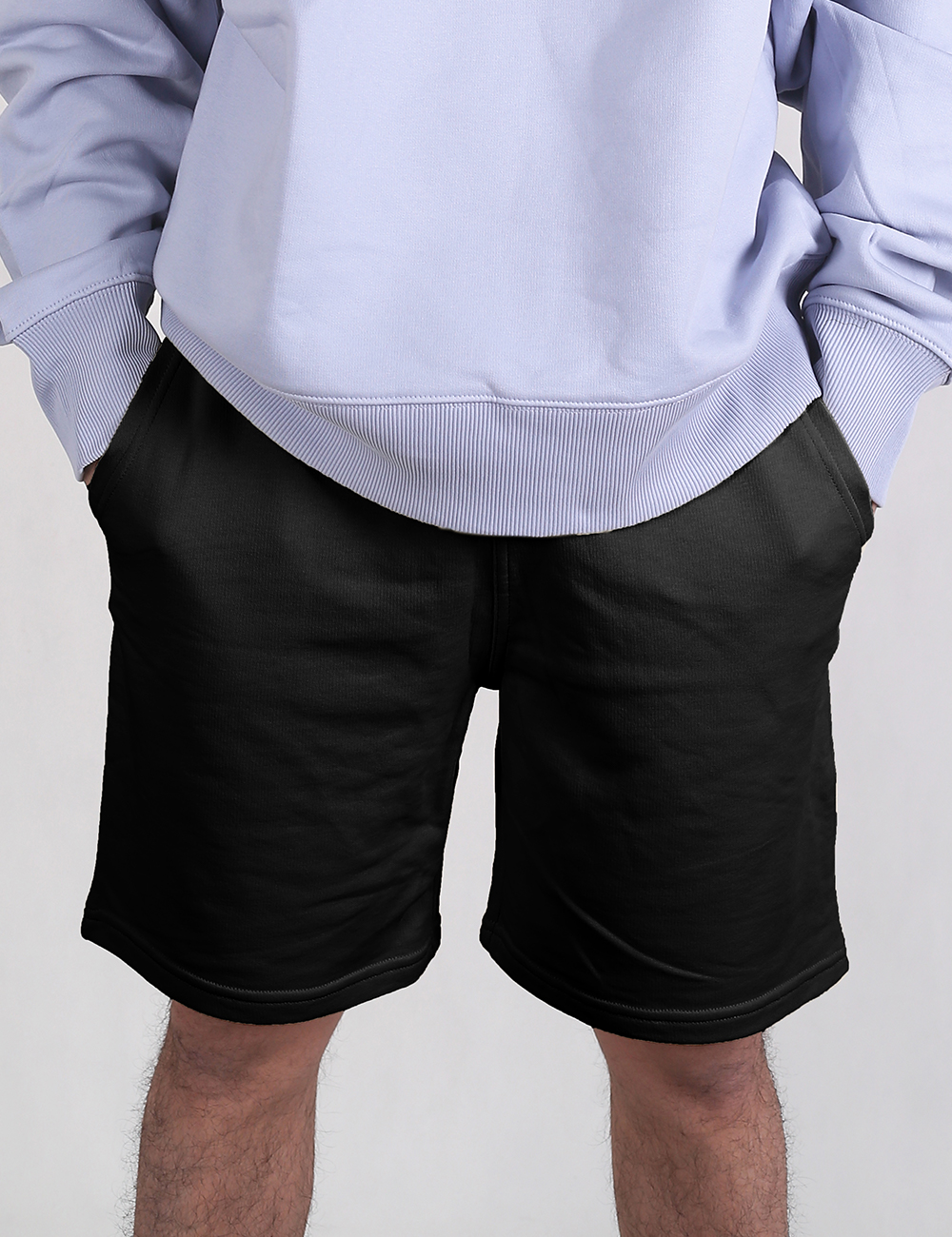 A front view of a person wearing a light lavender or pale blue crewneck sweatshirt paired with plain black sweat shorts.