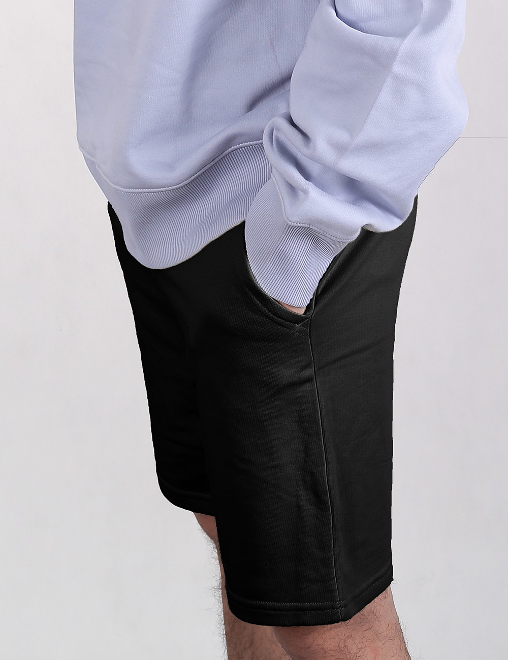 A close-up shot focuses on a person's hip and back pocket as they rest their right hand inside it. They are wearing black shorts and a light purple sweatshirt with a ribbed hem and cuffs.