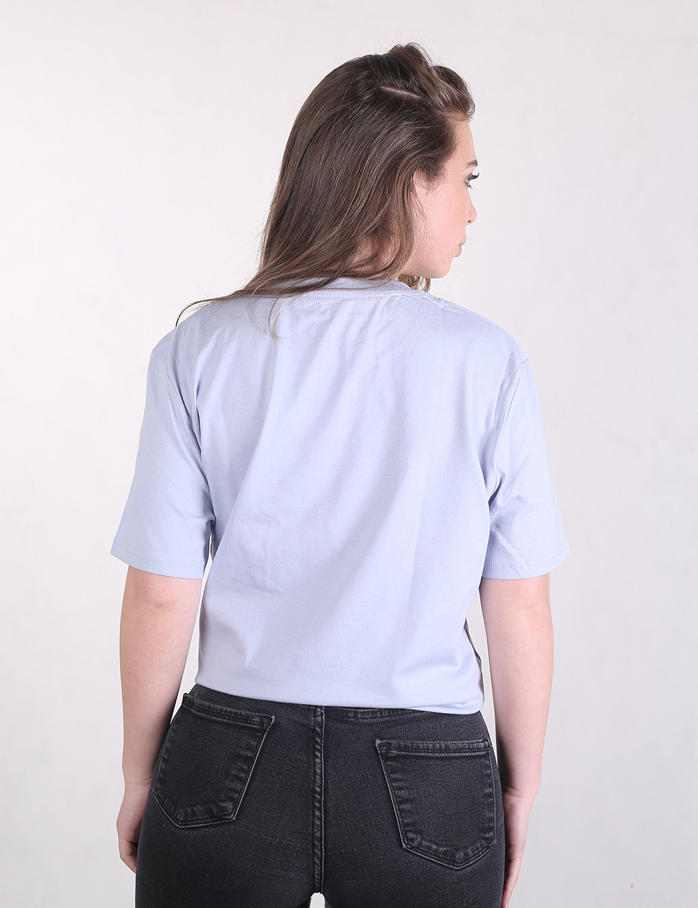 A woman seen from the back wearing a plain pastel blue short-sleeve t-shirt and black jeans.
