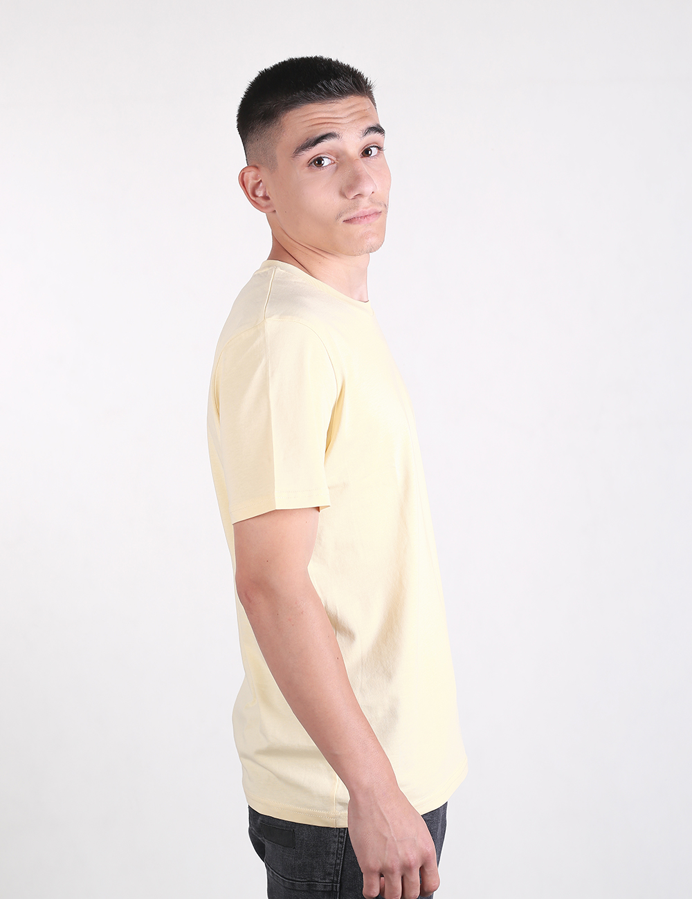 A man is wearing a plain, cream-colored crew neck t-shirt and dark gray or black jeans.