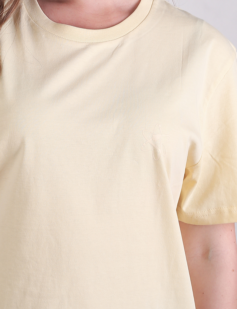 A close-up shot of a person wearing a light yellow, fine-ribbed crew neck t-shirt. The focus is on the upper chest and neckline of the short-sleeve top.