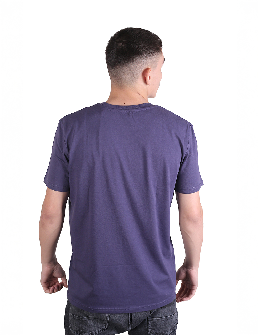 A man viewed from behind wearing a solid dark purple crew-neck t-shirt and grey jeans against a plain white background.