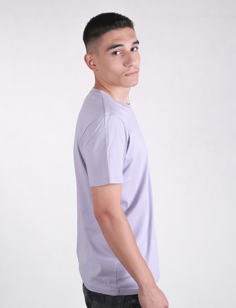 Side profile of a person wearing a light purple or lavender crewneck t-shirt with short sleeves and dark jeans, captured against a plain white background.
