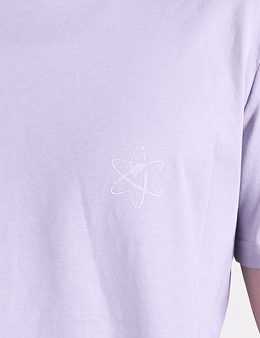 A close-up shot of a lavender-colored t-shirt featuring a small, white outline of an atom symbol printed on the left chest area.