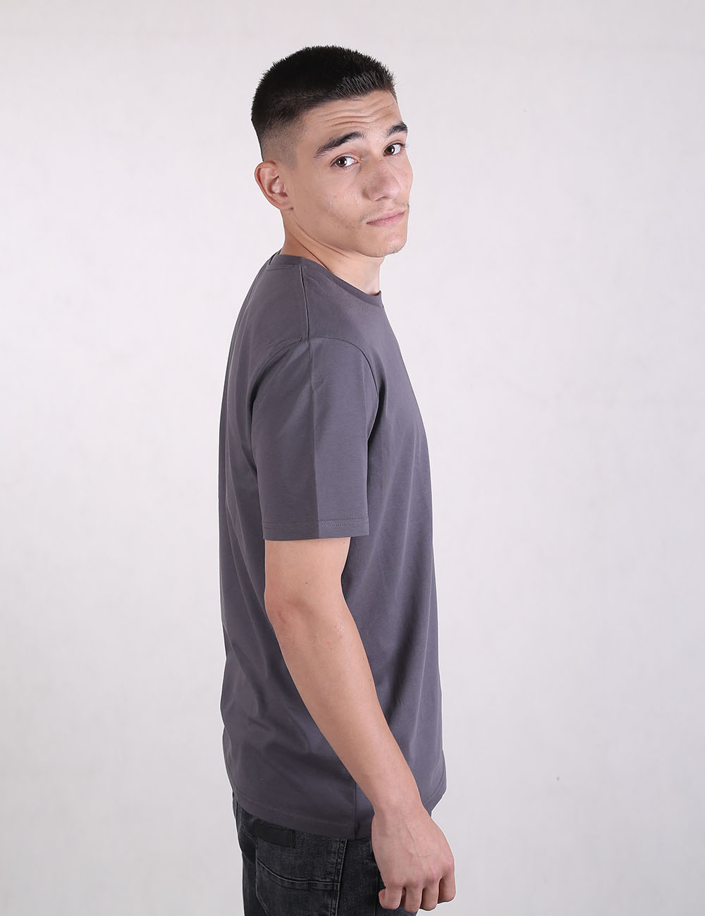 Rear view of a man with a short fade haircut, wearing a plain, solid charcoal grey t-shirt and black jeans against a light grey background.