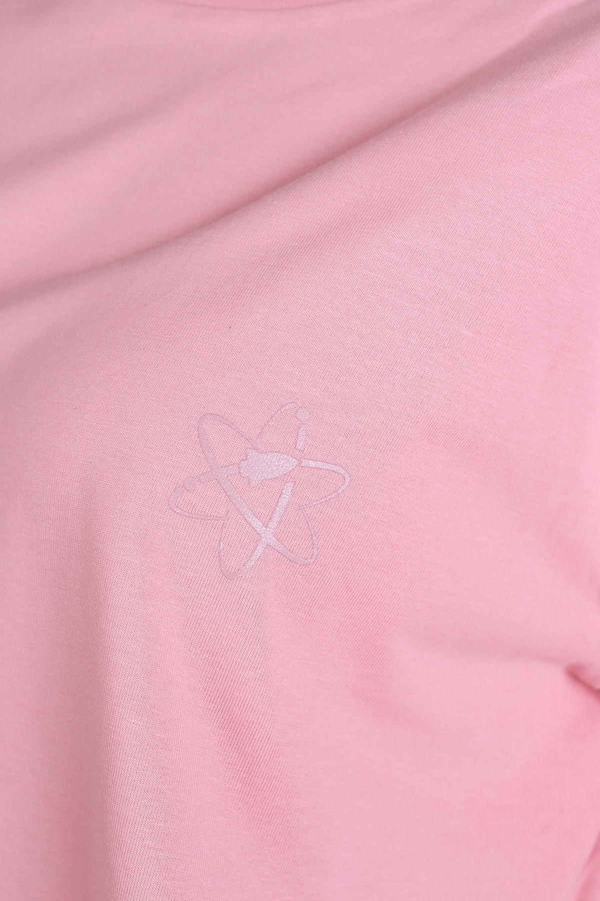 A close-up of a light pink fabric surface with a subtle, tonal embroidered Rocket  Science logo on the chest.