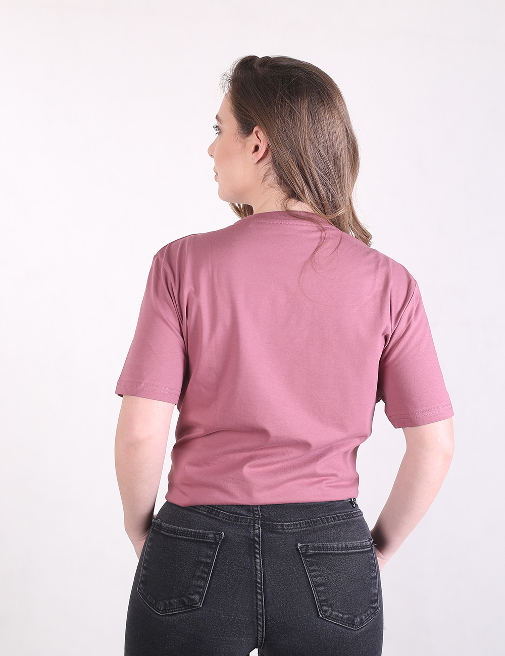 A woman facing away from the camera, wearing a mauve short-sleeve t-shirt tucked into dark-wash jeans.
