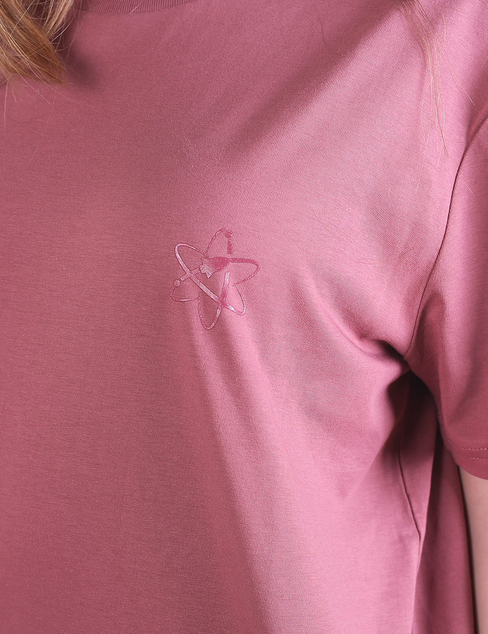 A close-up shot of a mauve-pink fabric featuring a small, embroidered atomic symbol logo on the chest area of the garment.