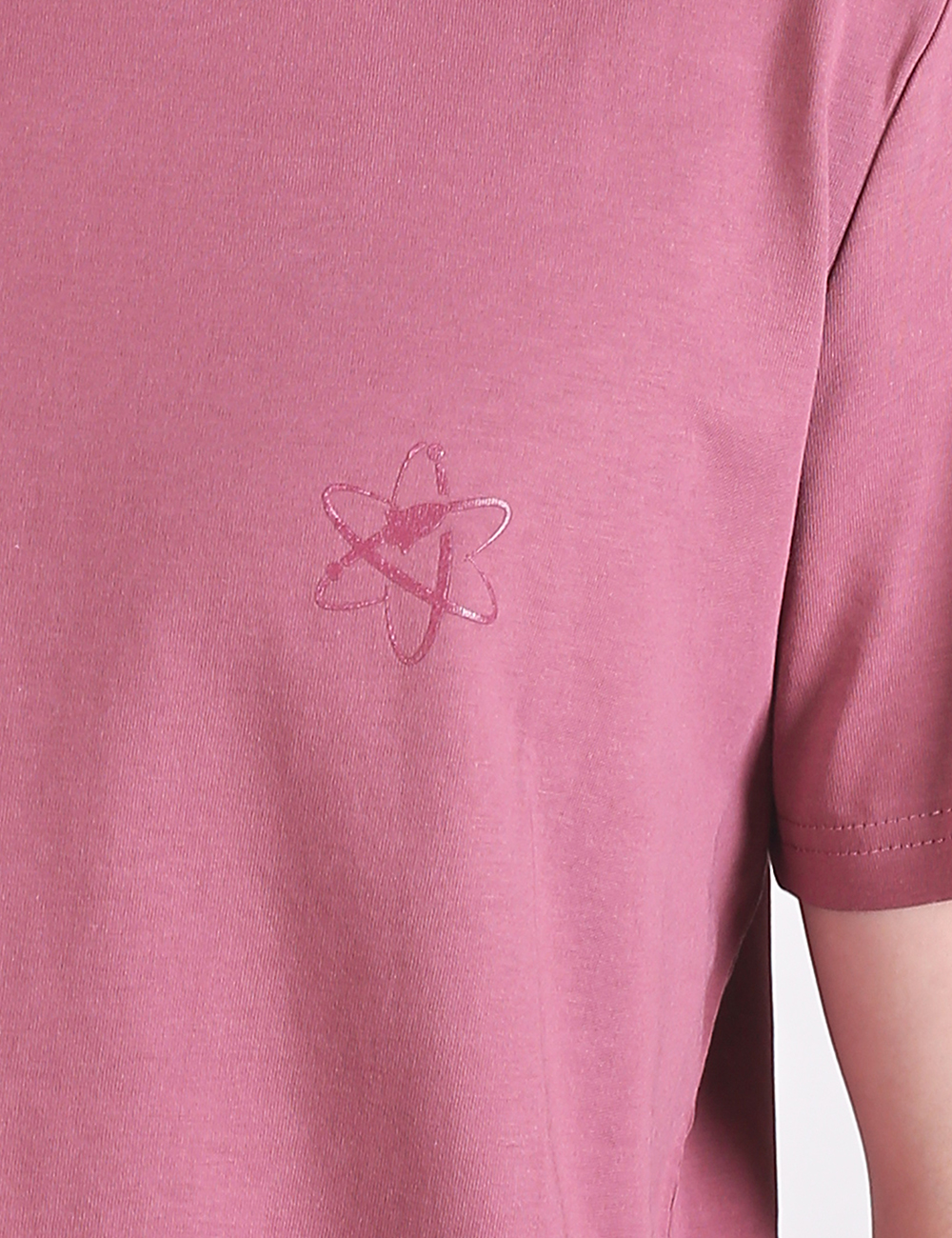 Close-up shot of a mauve pink t-shirt featuring a subtle, tonal embroidered or printed atom symbol on the left chest. The atom design consists of overlapping ellipses representing electron orbits surrounding a central nucleus. A portion of the right sleeve hem is visible on the right edge of the frame.