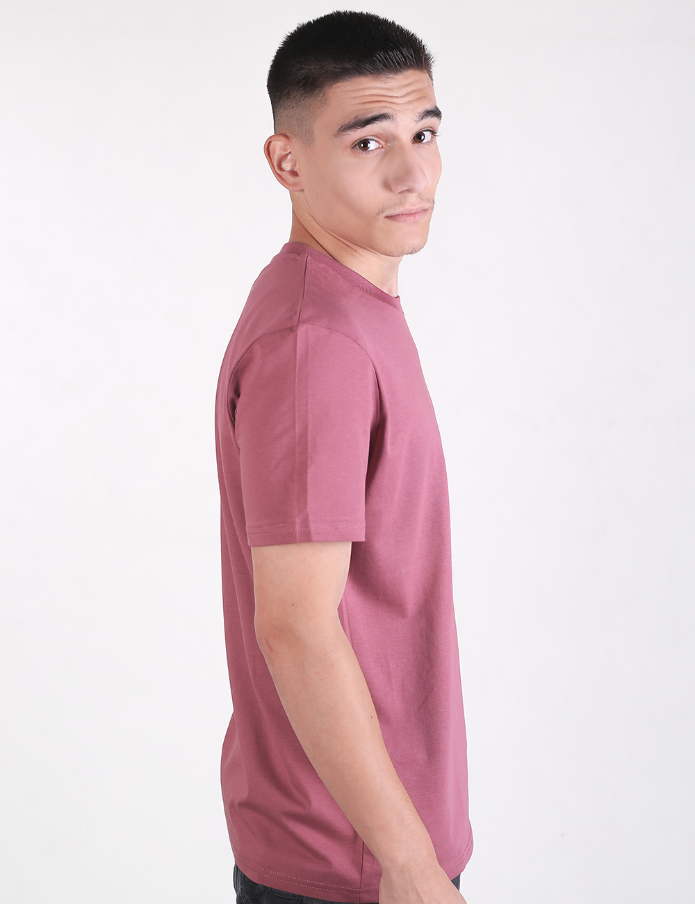 A man wearing a solid dusty pink short-sleeve crew neck t-shirt. The background is a clean, neutral off-white.