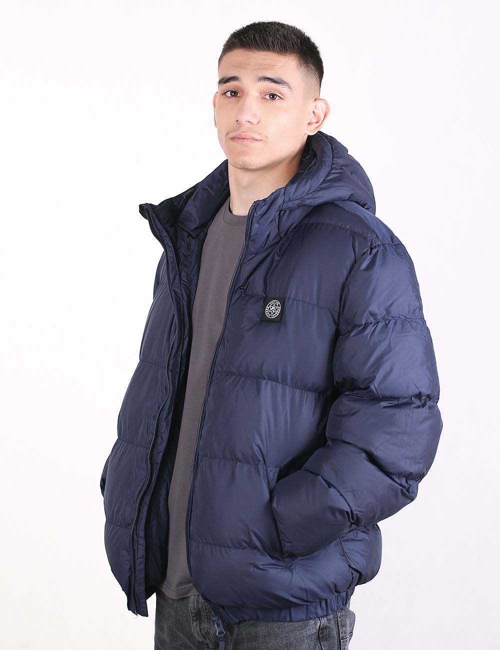 A man wearing a navy blue hooded puffer jacket over a dark gray t-shirt, photographed against a clean white studio background.