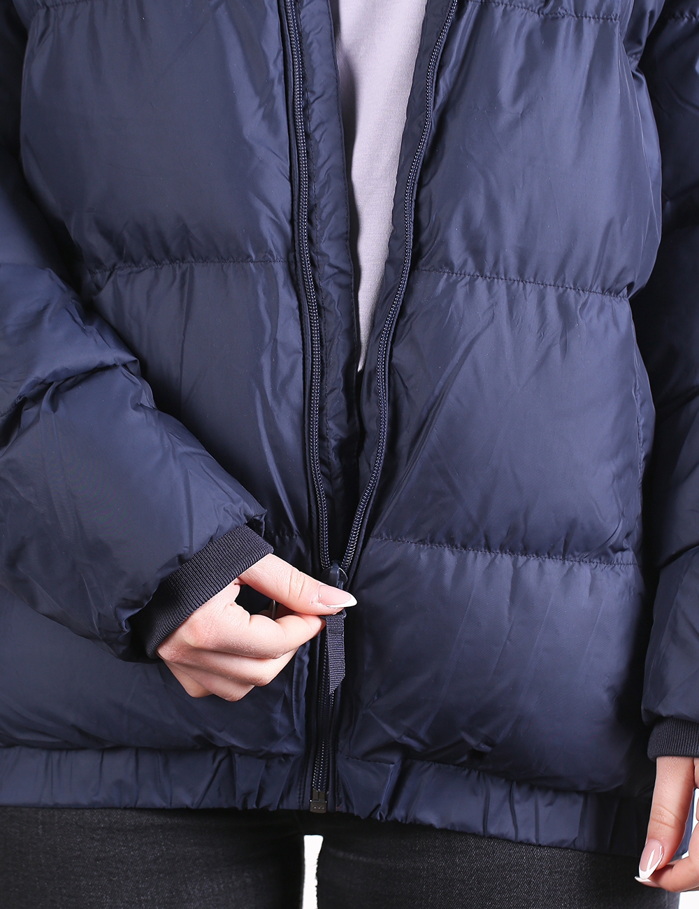 Close-up of a navy blue puffer jacket being zipped by a person, showing the front zipper, quilted stitching, and part of the hand adjusting the zipper tab.