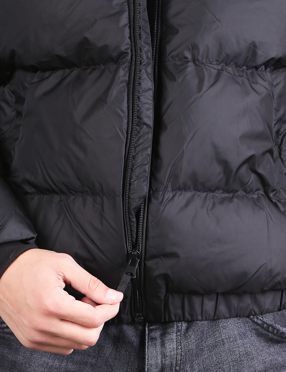 Close-up of a black puffer jacket being zipped, with a hand pulling the zipper tab and gray jeans visible below.