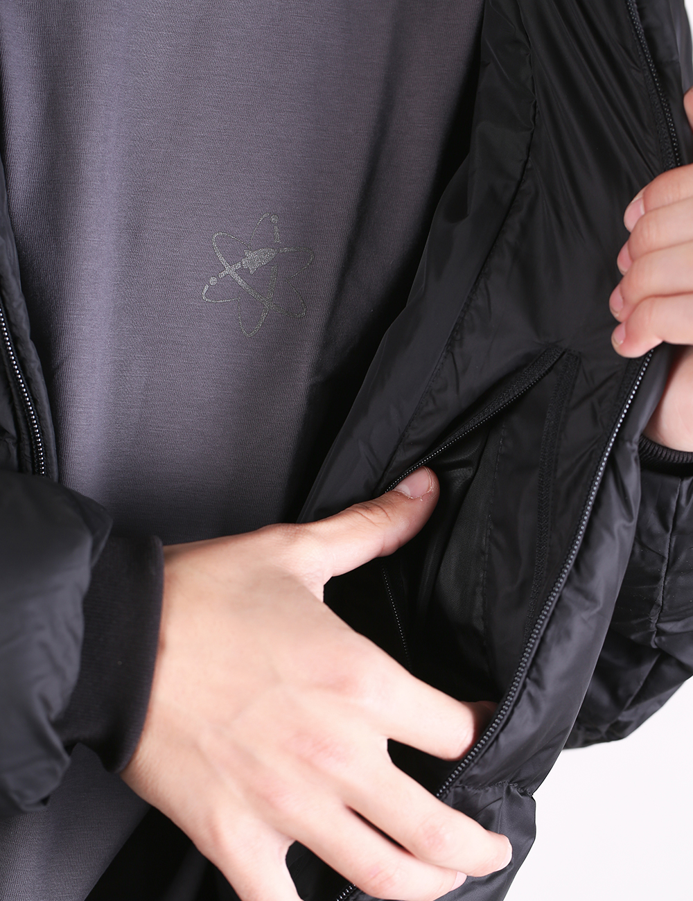 Close-up of a person wearing a black puffer jacket over a dark gray shirt, opening the jacket to show the interior pocket and zipper.