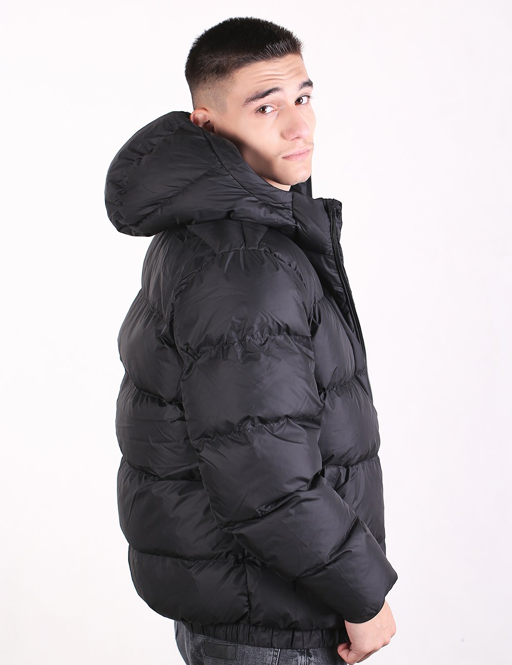 A man wearing a black puffer jacket with a high padded collar, shown from a side profile against a plain white background.