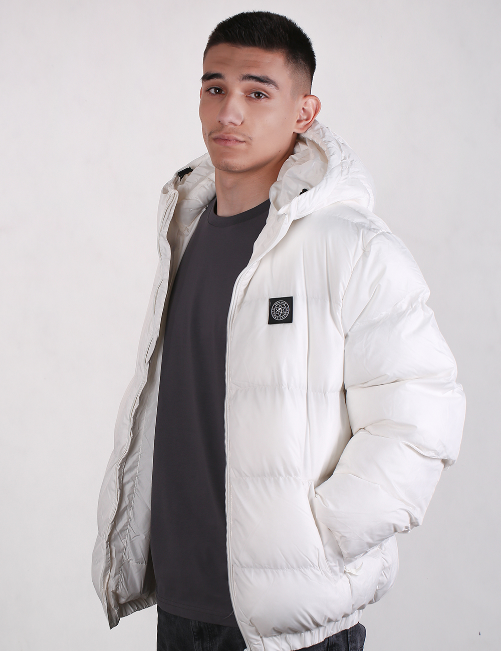 Man wearing a white puffer jacket with a brand logo on a plain background
