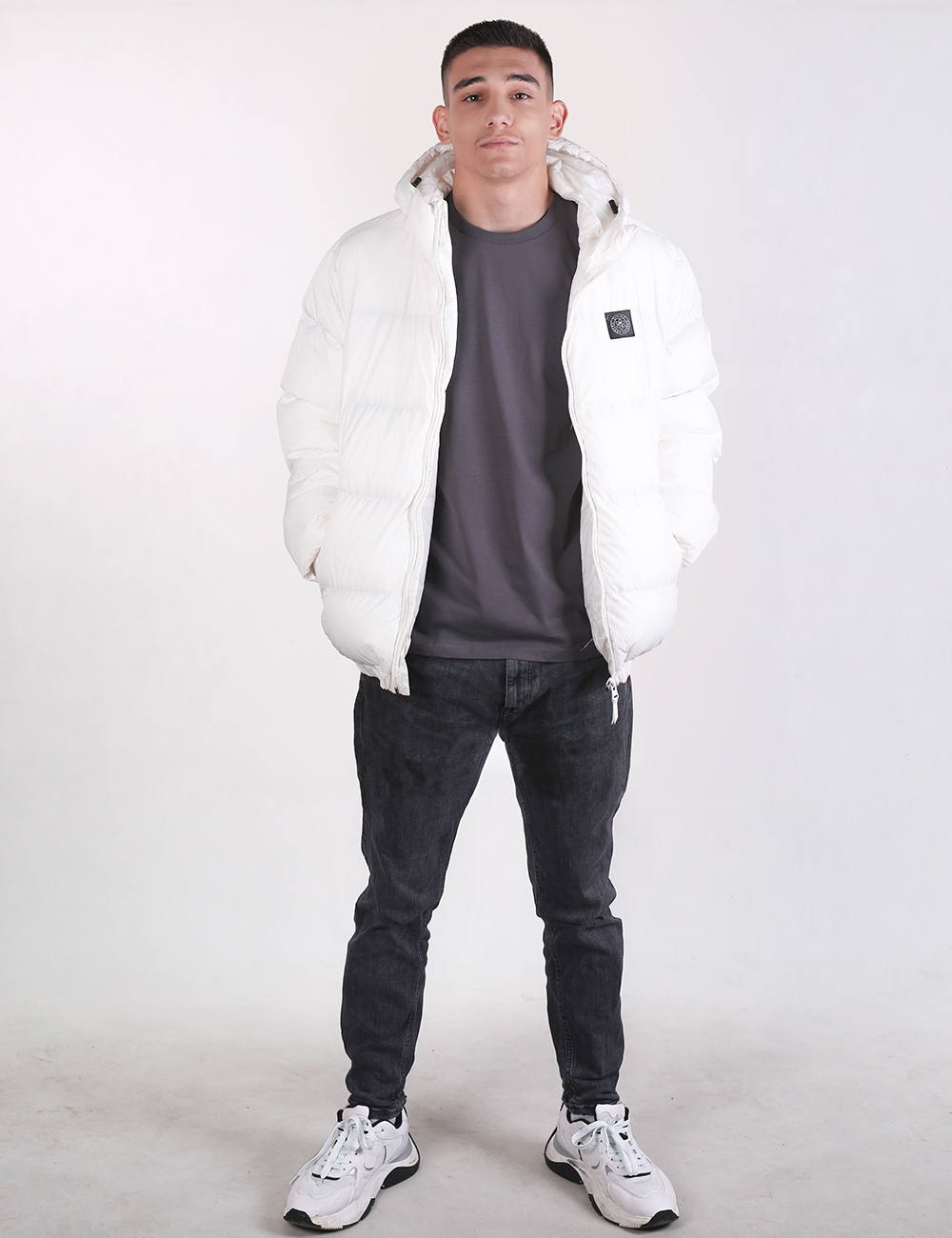 Person wearing a white puffer jacket, gray t-shirt, black jeans, and white sneakers on a white background