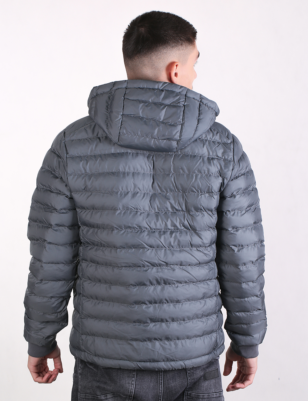 A man viewed from behind wearing a gray hooded puffer jacket, shown against a plain white studio background.