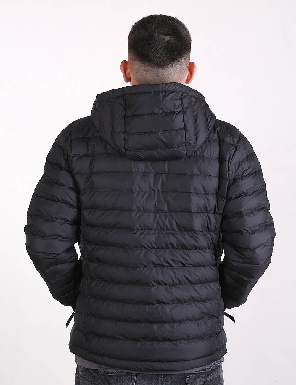 A man viewed from behind wearing a black hooded puffer jacket against a plain white background.