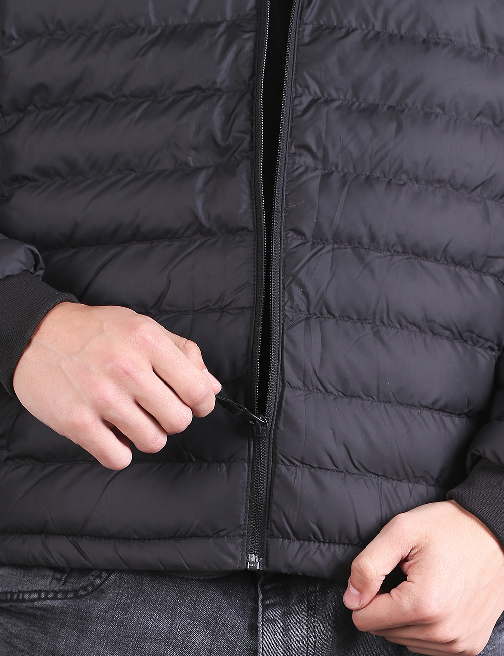 Close-up of a person wearing a black quilted puffer jacket, opening the front zipper with both hands.