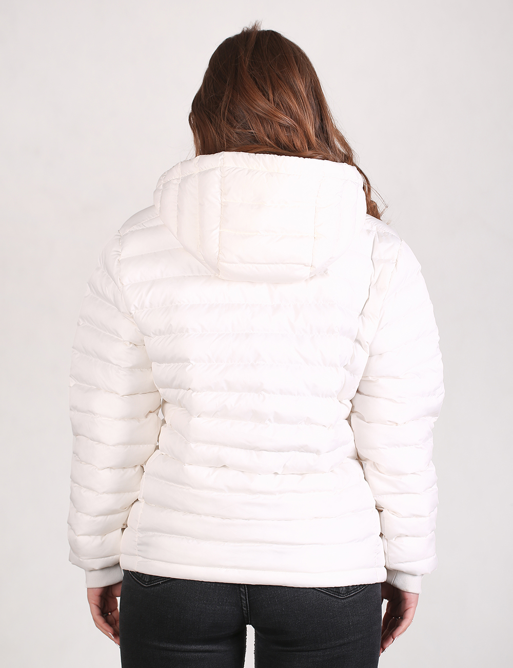 A woman viewed from the back wearing a white puffer jacket with horizontal quilting and a hood, paired with black pants, against a plain light background.