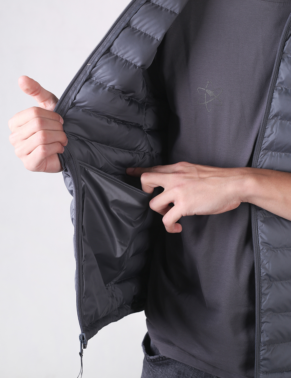 A person wears a dark gray puffy down vest open over a dark gray t-shirt.