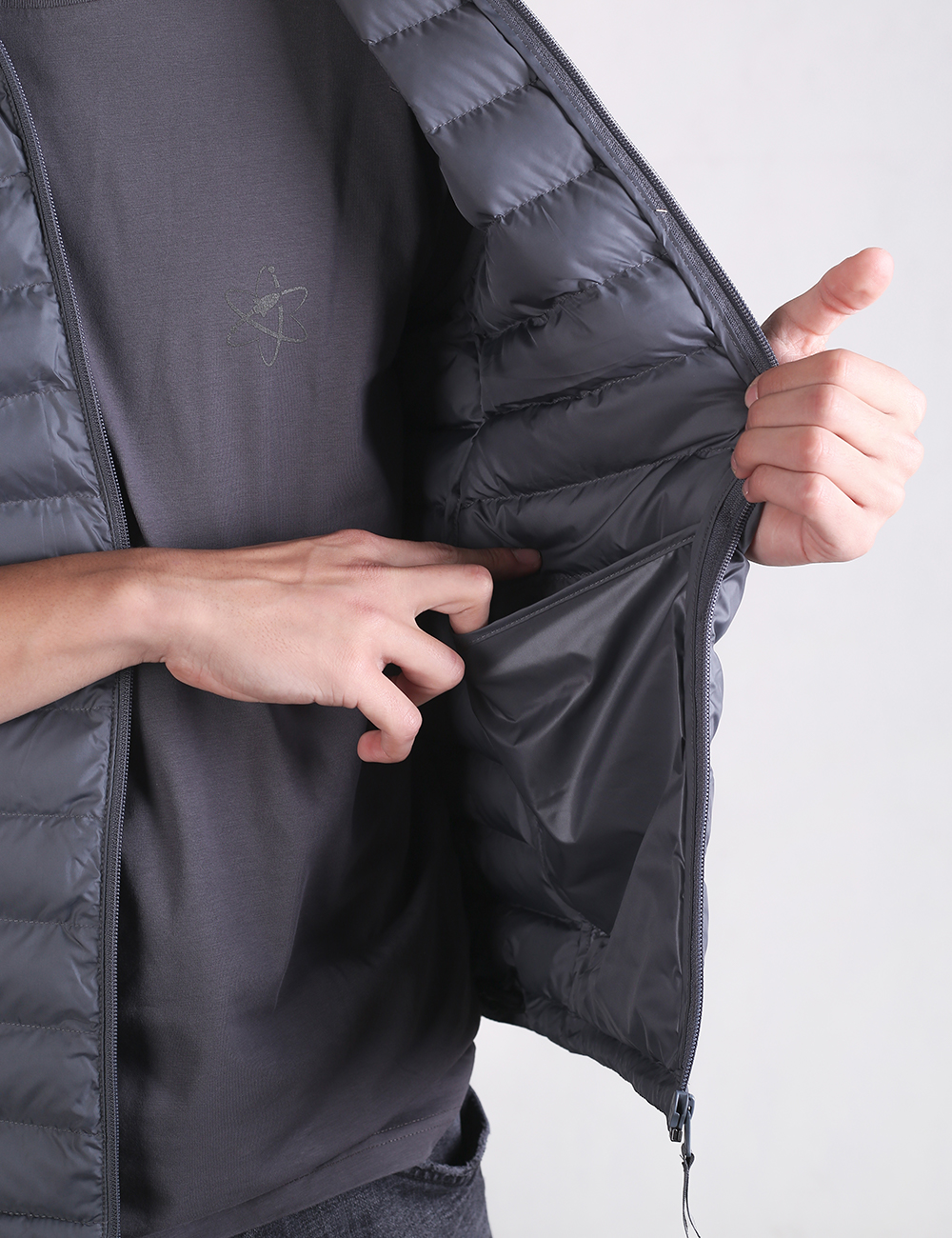 A person wears a dark gray puffy down vest open over a dark gray t-shirt.