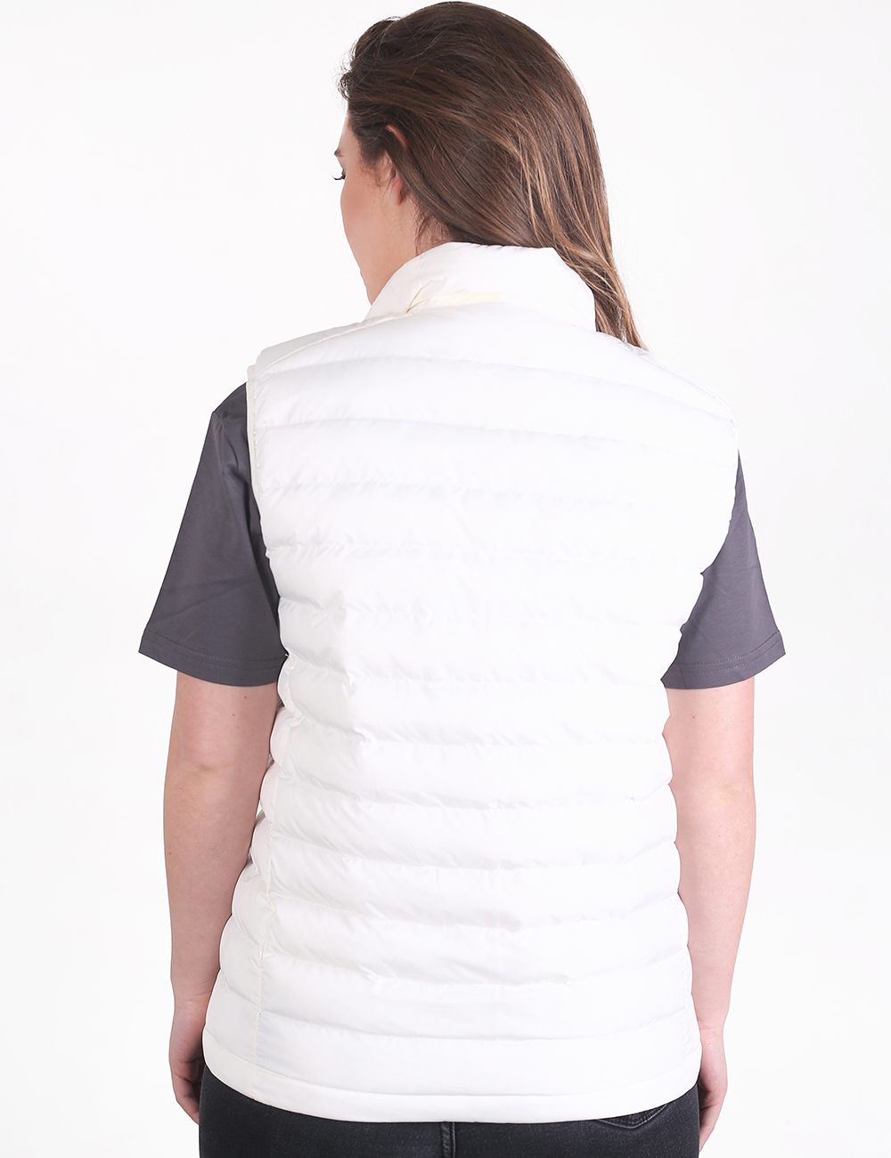 A woman viewed from the back wearing a white puffer vest over a dark gray short-sleeve shirt, against a plain white studio background.