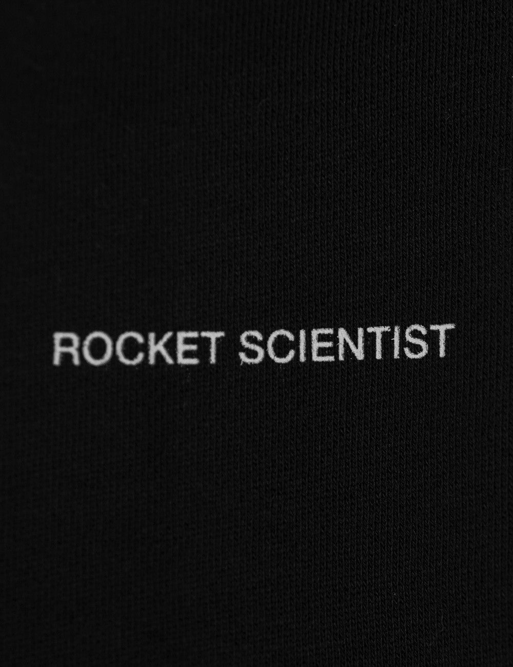 A close-up shot of a black fabric surface featuring the words "ROCKET SCIENTIST" printed horizontally across the center in a clean, white, all-caps sans-serif font.