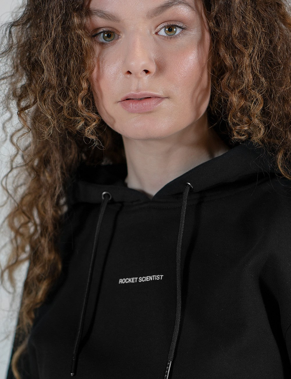 A close shot of  the Rocket Science unisex black Premium hoodie with ribbed cuffs, featuring a small print on the chest, styled casually with slim black jeans.