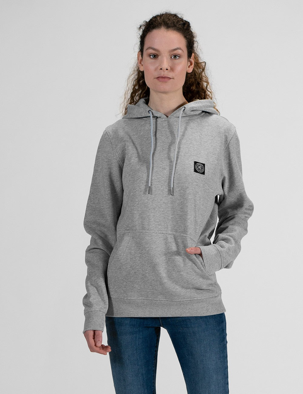 A front profile of a woman with long, curly brown hair wearing a grey hoodie and blue jeans.