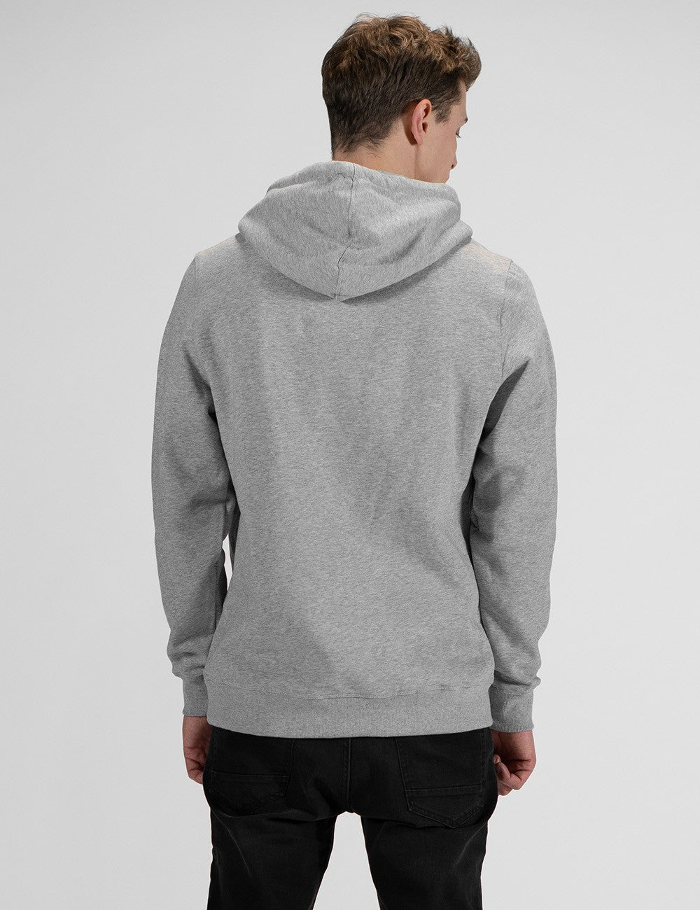 A man seen from behind wearing a heather grey pullover hoodie and black pants against a light grey background.