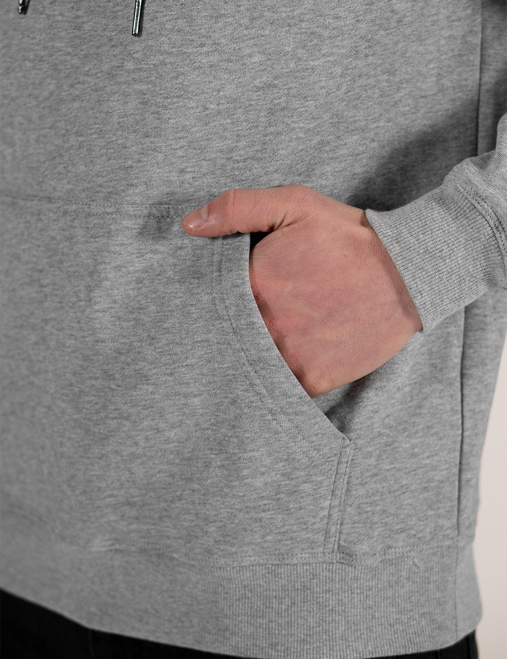 A close-up shot of a person wearing a heather grey pullover hoodie, with their right hand resting inside the front kangaroo pocket.