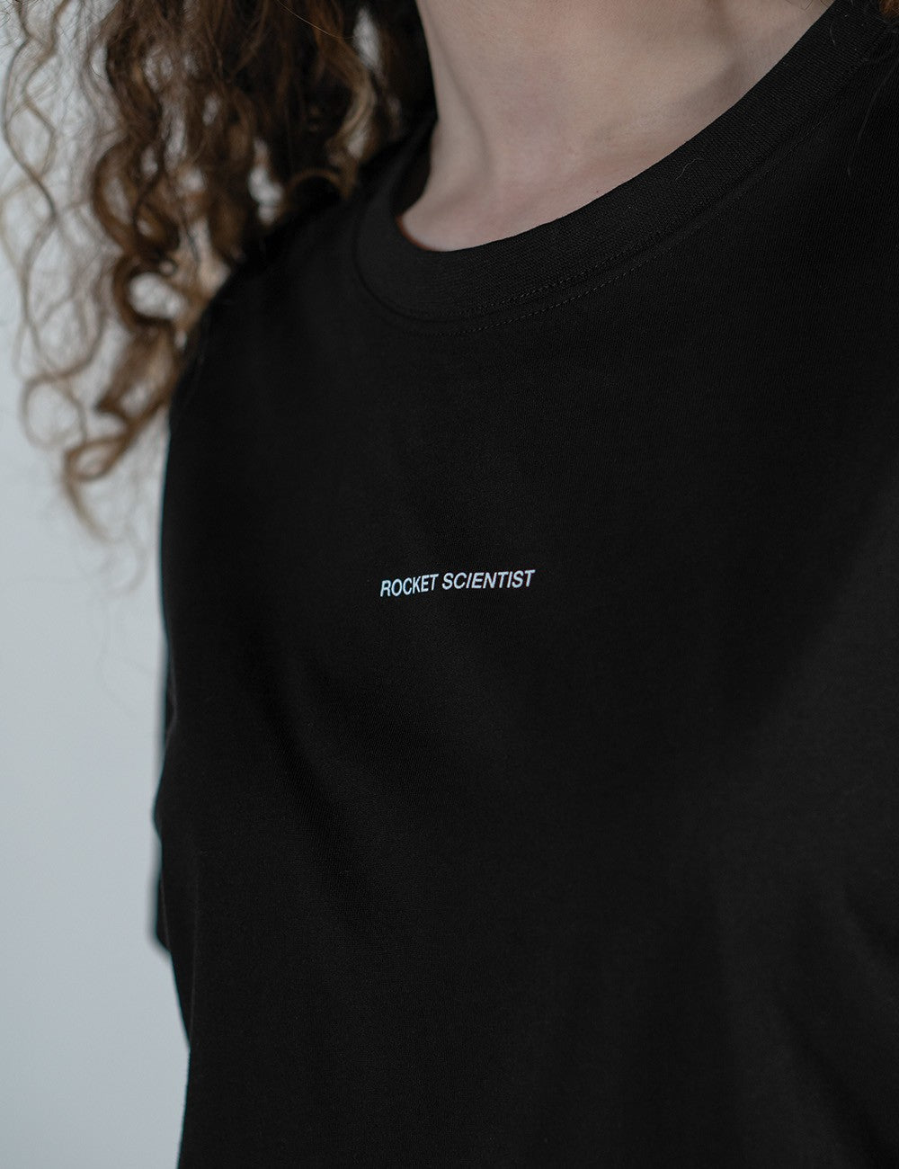 Woman showcasing a black round-neck T-shirt with the words “Rocket Scientist” on the front.
