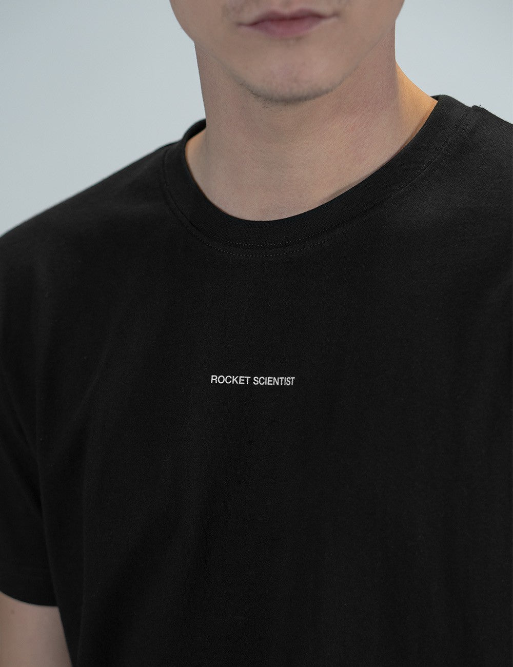 Man showcasing a black round-neck T-shirt with the words “Rocket Scientist” on the front.