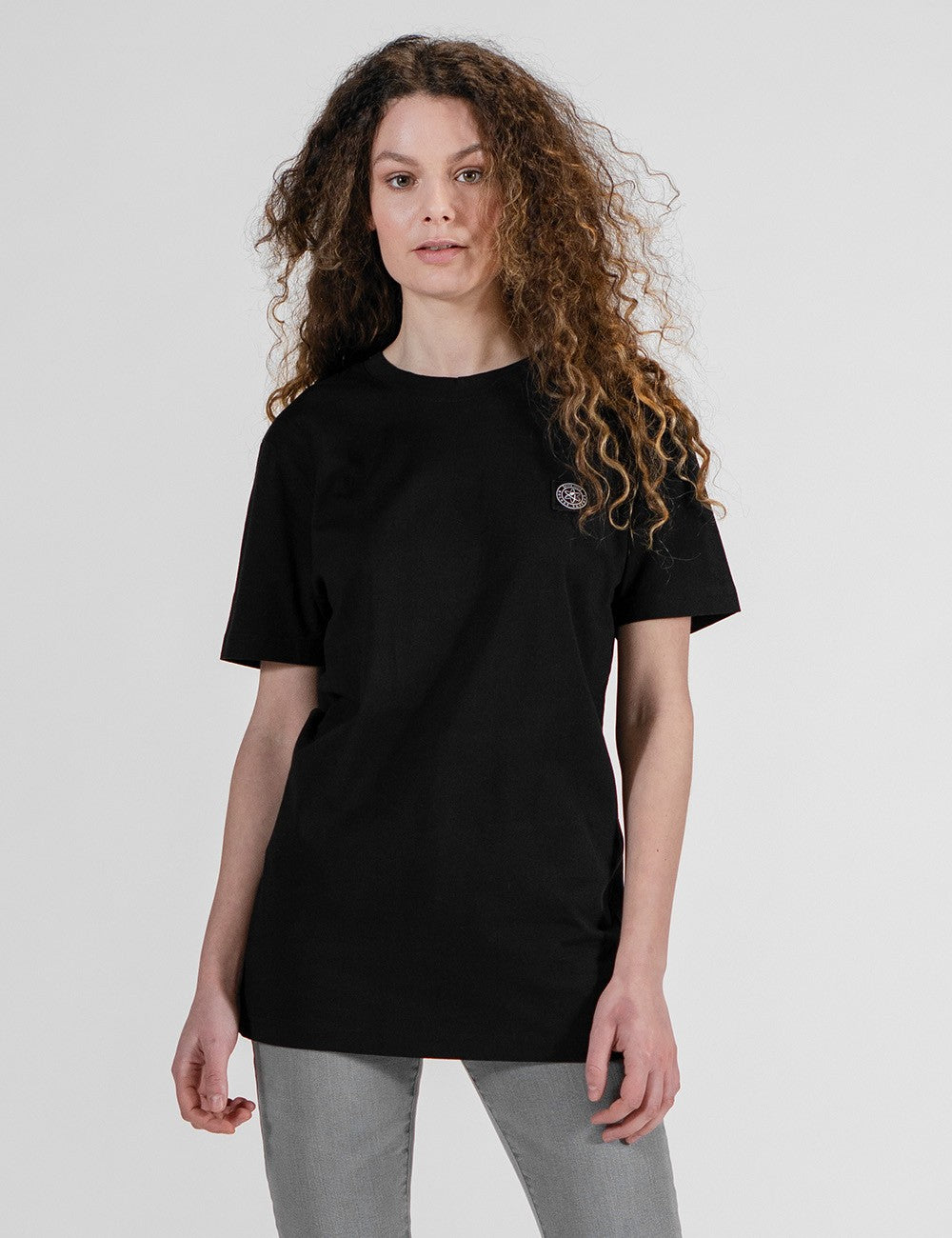 This image shows a girl wearing a black crew-neck t-shirt with a small logo patch on the chest.