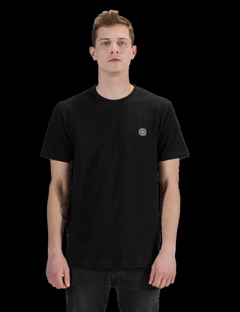 A man with short brown hair stands against a plain grey background, wearing a simple black short-sleeve crewneck t-shirt with a small, minimalist logo print "Icon" on the left side of the chest, paired with black pants.